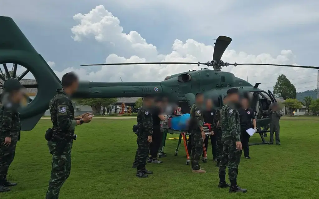 Military personnel gather beside a helicopter on a grassy field.