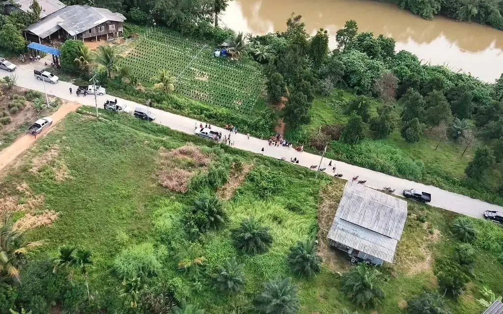 Aerial view of a rural road, fields, houses, vehicles, and a river.