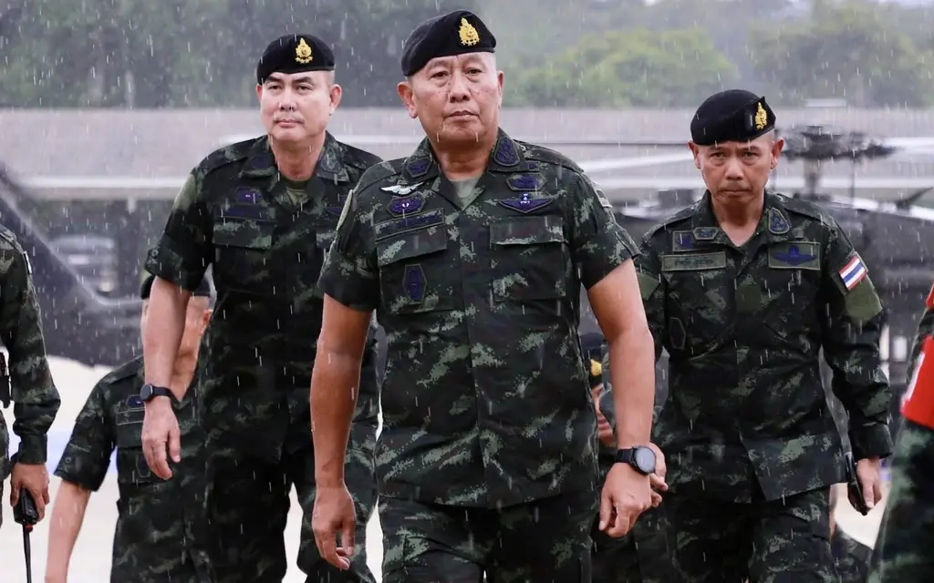Thai military officers in camouflage walking outdoors in the rain.
