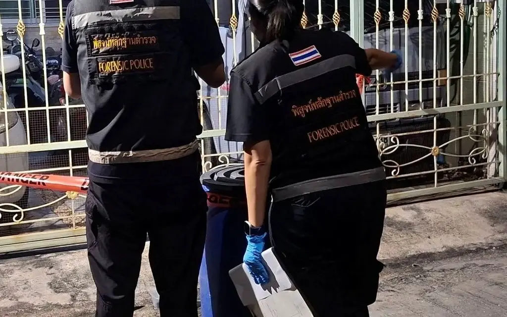 Forensic police officers inspect a gated Bangkok house at night.