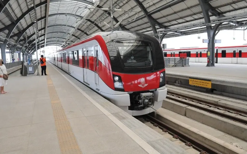 Red and white commuter trains at a covered railway station platform.