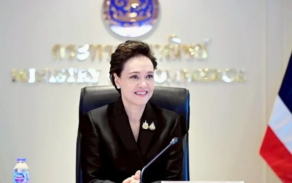 Woman chairs a meeting beside a Thai flag.